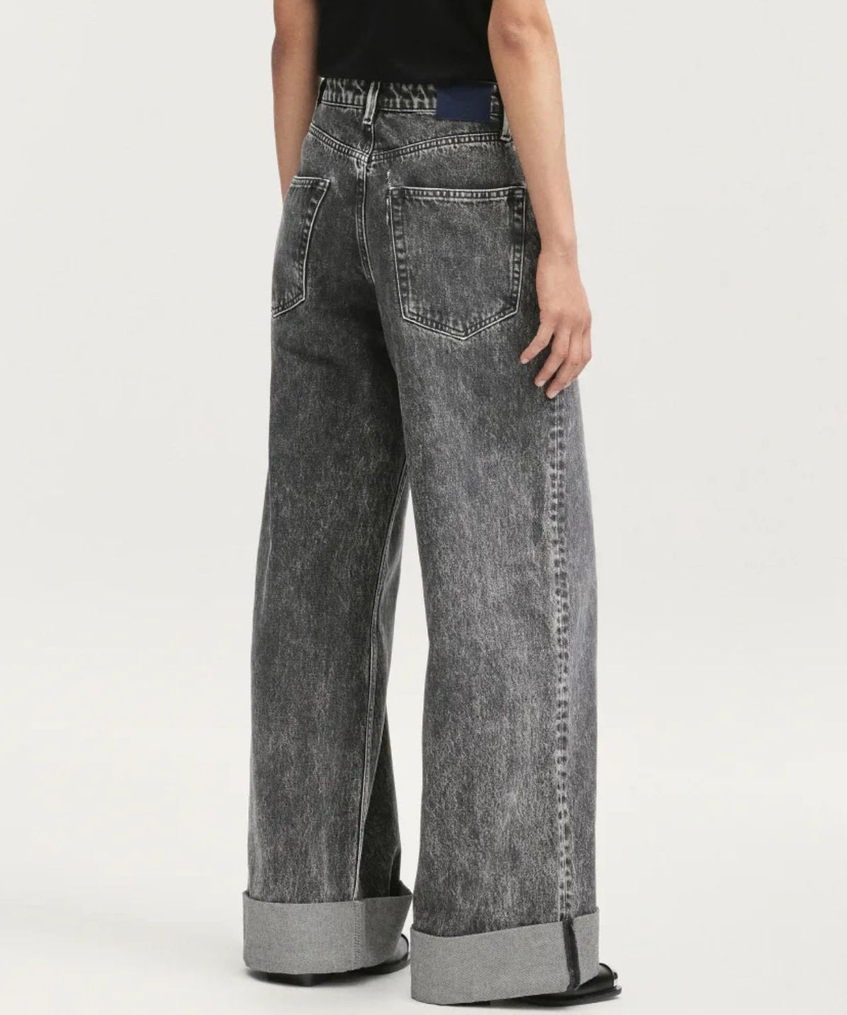 Person wearing black acid-wash jeans on a white background