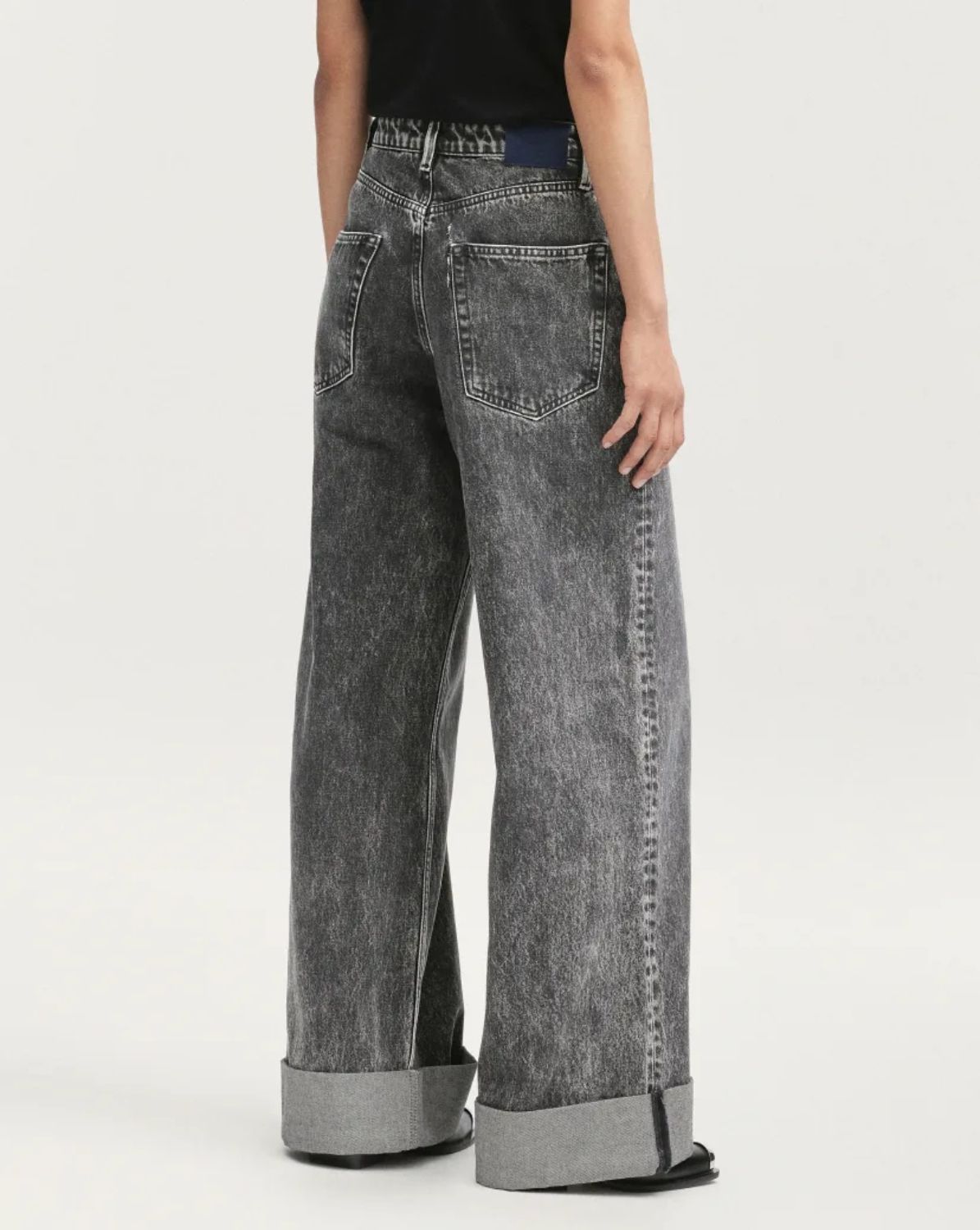 Person wearing black acid-wash jeans on a white background