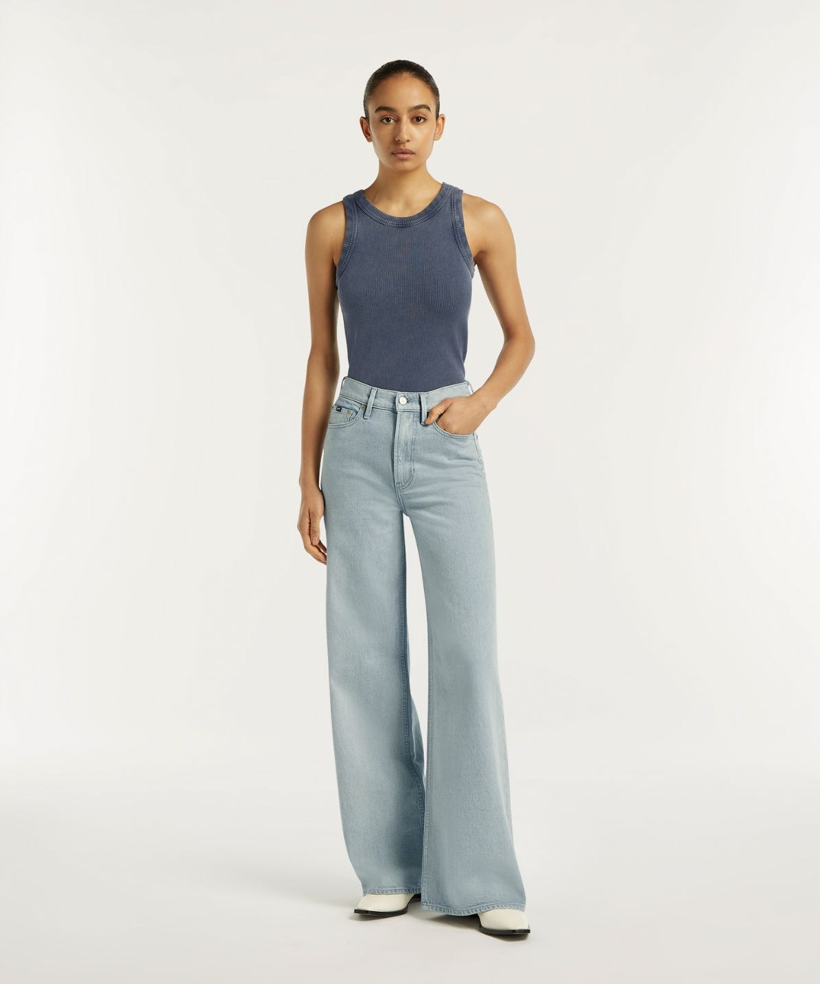 Woman wearing a blue sleeveless top and light blue jeans on a white background