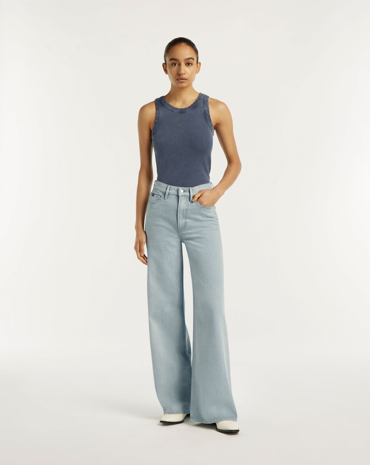 Woman wearing a blue sleeveless top and light blue jeans on a white background